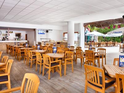 Bright dining area with wooden chairs and tables, some with umbrellas outside.