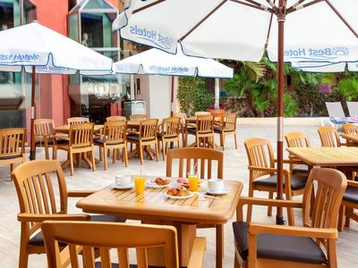 Terrace with wooden tables and chairs, umbrellas, and set tables in daylight.