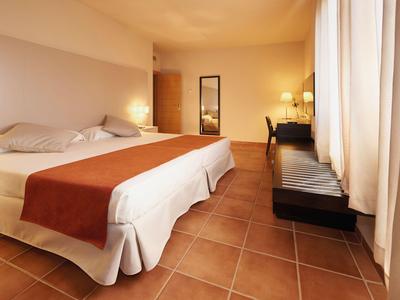 Brightly furnished hotel room with large bed and desk by the window.