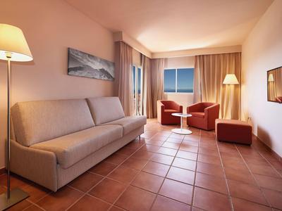 Bright living room with sofa, armchairs, floor lamps, and tiled floor.