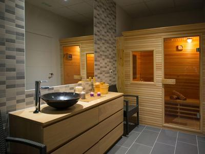 Nowoczesna sauna z drewnianą obudową, podświetlanym lustrem i umywalką na komodzie.