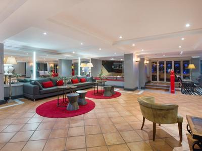 Nowoczesna lobby hotelowa z czerwonymi dywanami, szarymi siedzeniami i ciepłym oświetleniem.