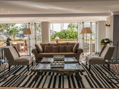 Nowoczesny salon hotelowy z brązową kanapą, fotelami i dużymi oknami na taras na zewnątrz.