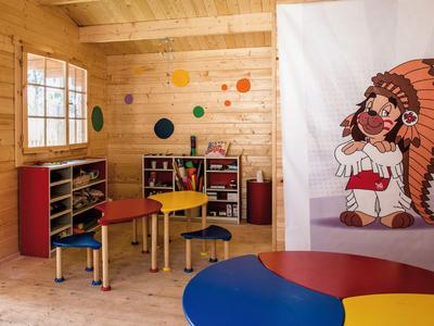 Kolorowy pokój zabaw dla dzieci z drewnianymi ścianami, kolorowymi stołami i kreskówkową dekoracją na ścianie.