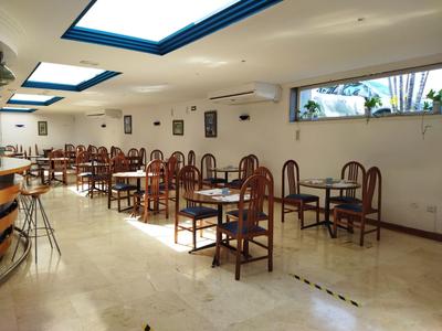 Heller Speisesaal mit Holzstühlen und Tischen, großen Fenstern und Deckenfenstern.