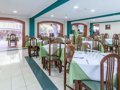 Restaurant lumineux avec des tables et chaises en bois, dressées avec des nappes blanches et vertes.