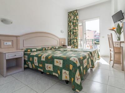 Chambre d'hôtel lumineuse avec lit double, table de chevet, bureau et balcon avec vue sur la ville.