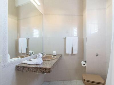 Salle de bains lumineuse avec plan de travail en granit, miroir et serviettes blanches au mur.