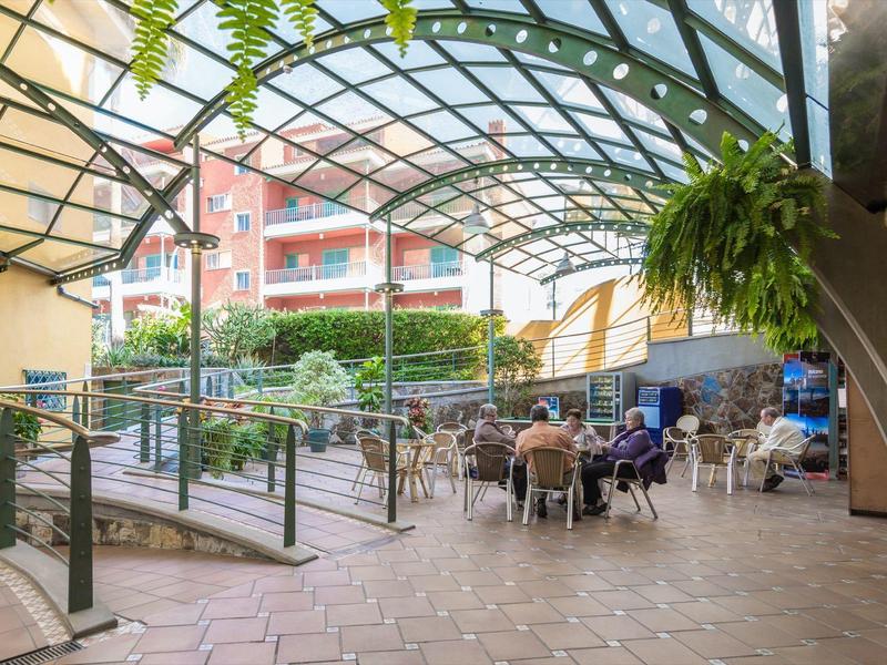 Lounge esterna coperta con area salotto, piante e vista su un edificio dell'hotel.