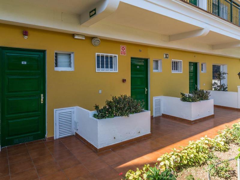 Vista esterna di un edificio giallo con porte verdi e fioriere bianche su una terrazza.