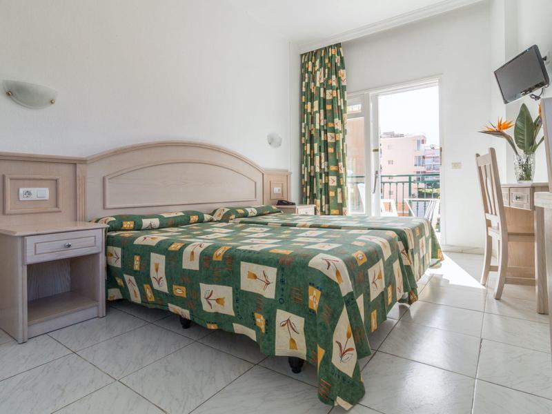 Camera d'albergo luminosa con letto matrimoniale, balcone e TV a muro.