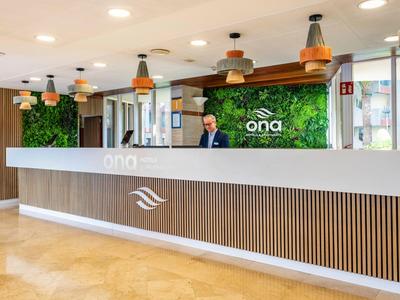 Nowoczesna recepcja hotelowa z białym biurkiem i zieloną ścianą roślin w tle.