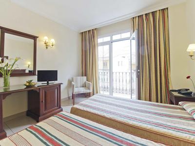 Camera d'hotel luminosa con due letti singoli, scrivania, sedia e grande finestra con tende.