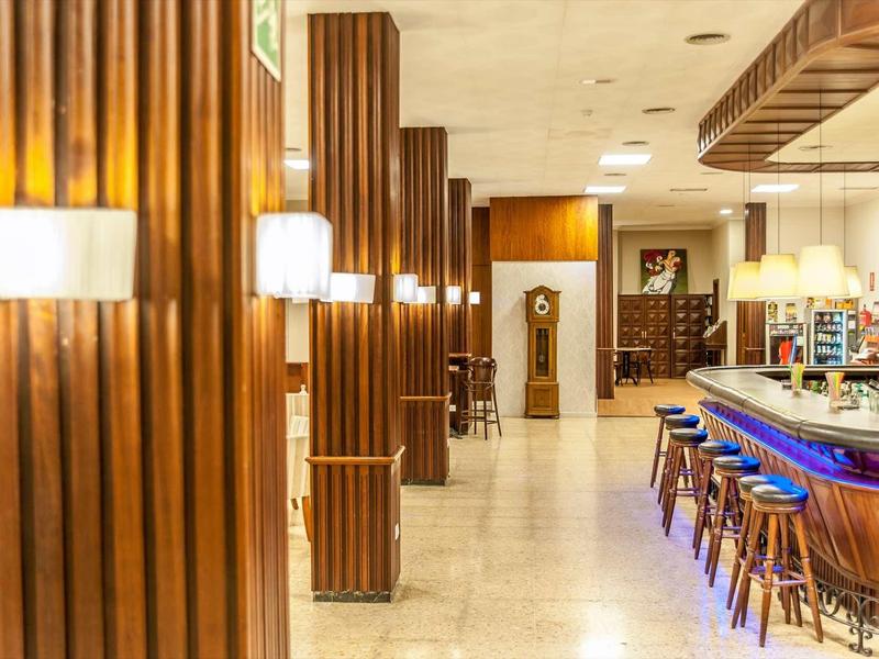 Innenraum einer Bar mit Holzvertäfelungen, hellen Wänden, modernen Lampen und hoher Bartheke.