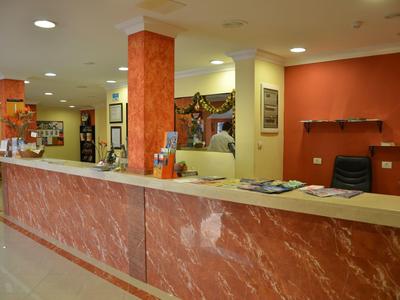 Rezeption mit rotem Marmortresen, beleuchteten Deckenspots und Wanddekoration in hellem Raum.