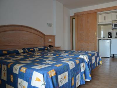 Pokój hotelowy z dwoma łóżkami, niebieską pościelą w wzory i małym aneksem kuchennym w tle.