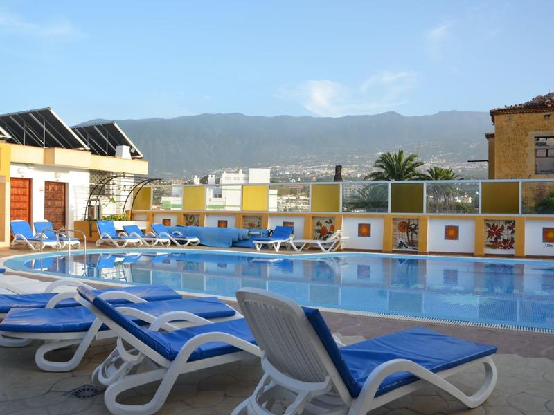 Buitenzwembad met blauwe ligstoelen, gele muren en bergen op de achtergrond.