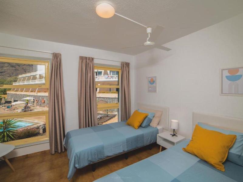 Schlafzimmer mit zwei Einzelbetten, blauen Decken, gelben Kissen, zwei Fenstern und weißen Wänden.