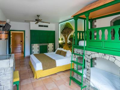 Chambre d'hôtel avec lit double, lit superposé vert, murs en pierre et sol en terre cuite.
