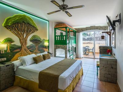 Chambre d'hôtel moderne avec lit double, art mural et terrasse avec vue sur le jardin.