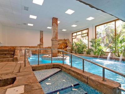 Espace piscine intérieure avec pierres naturelles, jacuzzi et grandes fenêtres donnant sur des plantes.