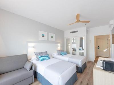 Chambre d'hôtel bien éclairée avec deux lits simples, un canapé et un ameublement moderne.