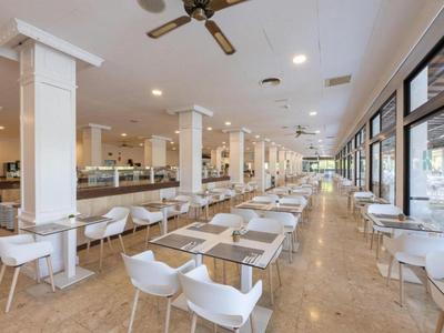 Salle à manger spacieuse et lumineuse avec des chaises blanches et de grandes fenêtres sur un côté.