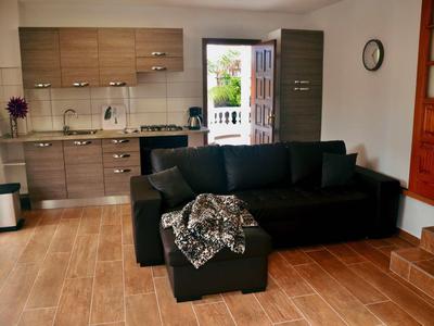 Offenes Wohnzimmer mit schwarzem Sofa, Holzfußboden und moderner Küche in neutralen Farben.