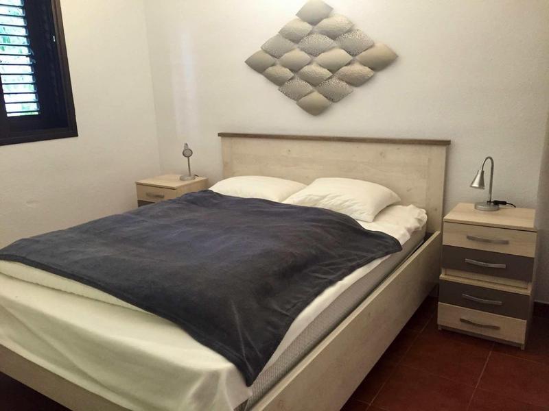 Schlafzimmer mit großem Bett, zwei Nachttischen, grauer Bettdecke und dekorativem Wandbild.