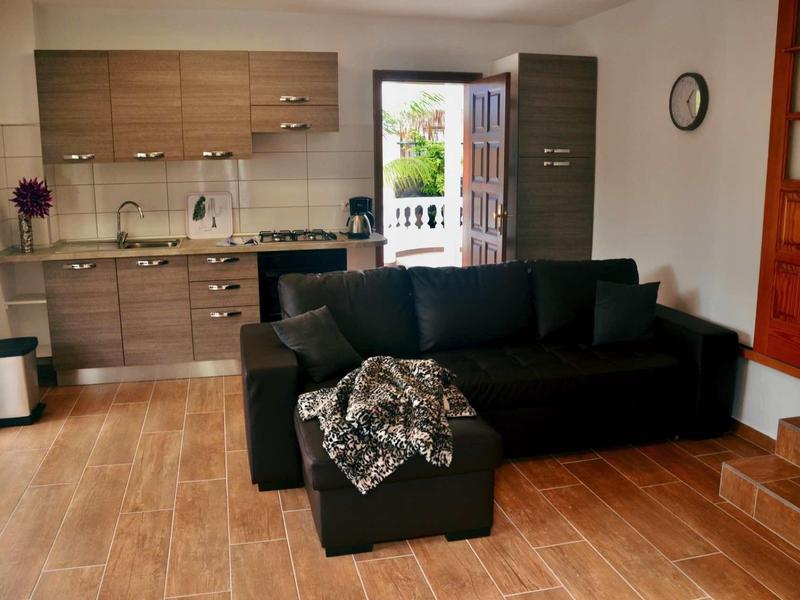 Offenes Wohnzimmer mit schwarzem Sofa, Holzfußboden und moderner Küche in neutralen Farben.