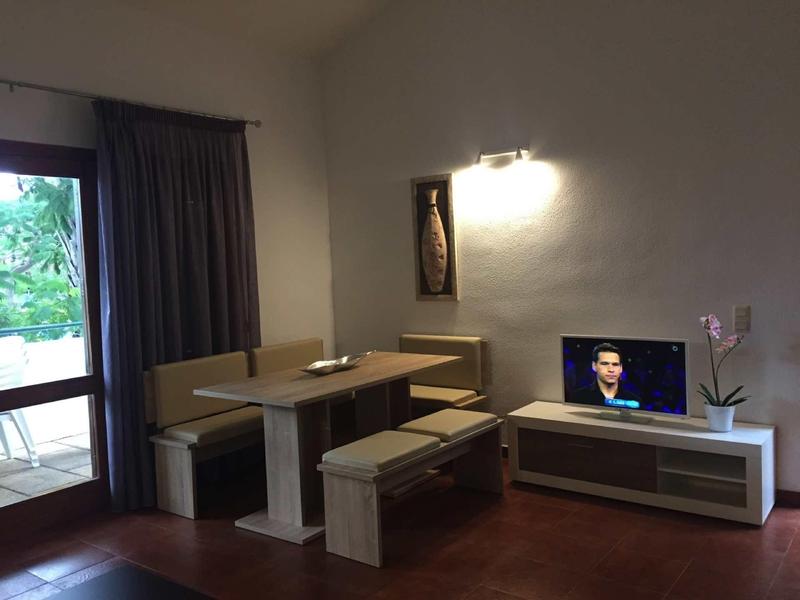 Gemütliches Wohnzimmer mit Bank und Tisch, Fernseher und Fenster mit Blick ins Grüne.