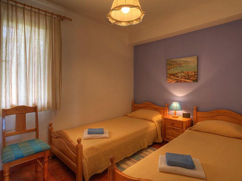 Kleines Schlafzimmer mit zwei Einzelbetten, Holzmöbeln, lila Wand und Tageslicht durch Fenster.