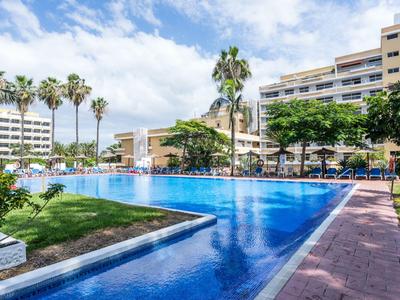 Grand bassin d'hôtel avec surface d'eau bleue, entouré de palmiers et de bâtiments modernes.