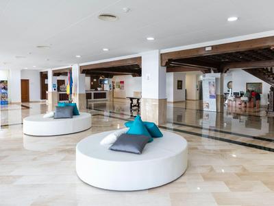 Hall d'hôtel lumineux avec des bancs blancs circulaires et des coussins bleus sur un sol en marbre brillant.