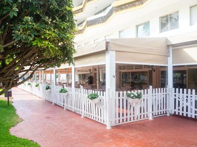 Un hôtel avec une terrasse entourée d'une clôture blanche et d'un auvent.