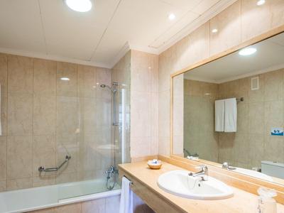 Salle de bain lumineuse avec baignoire, douche en verre, serviettes et grand miroir au-dessus du lavabo.
