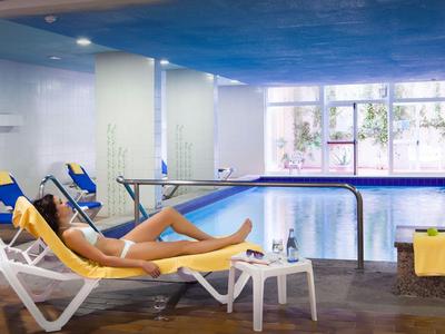 Piscine intérieure avec chaises longues, murs bleus et grande fenêtre donnant sur des plantes.