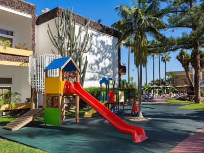 Aire de jeux enfantine colorée avec toboggan et structures d'escalade dans le jardin de l'hôtel sous des palmiers.