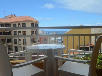 Balkon mit Tisch und zwei Stühlen mit Blick auf Gebäude und das Meer im Hintergrund.