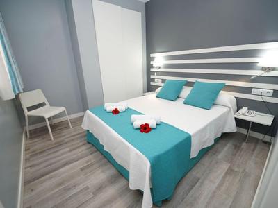 Modernes Hotelzimmer mit Doppelbett, blauer Bettdecke und zwei weißen Nachttischen.