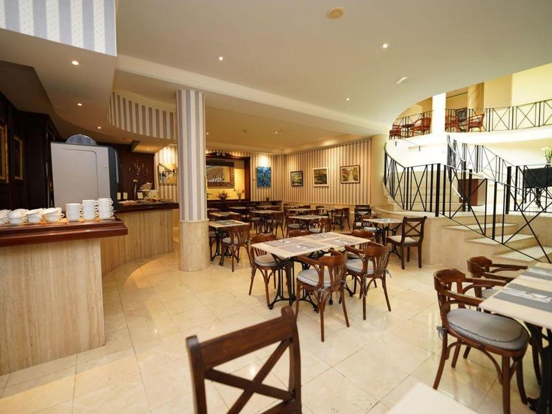 Světlá a moderní hotelová restaurace s mnoha dřevěnými stoly a židlemi a otevřeným schodištěm.