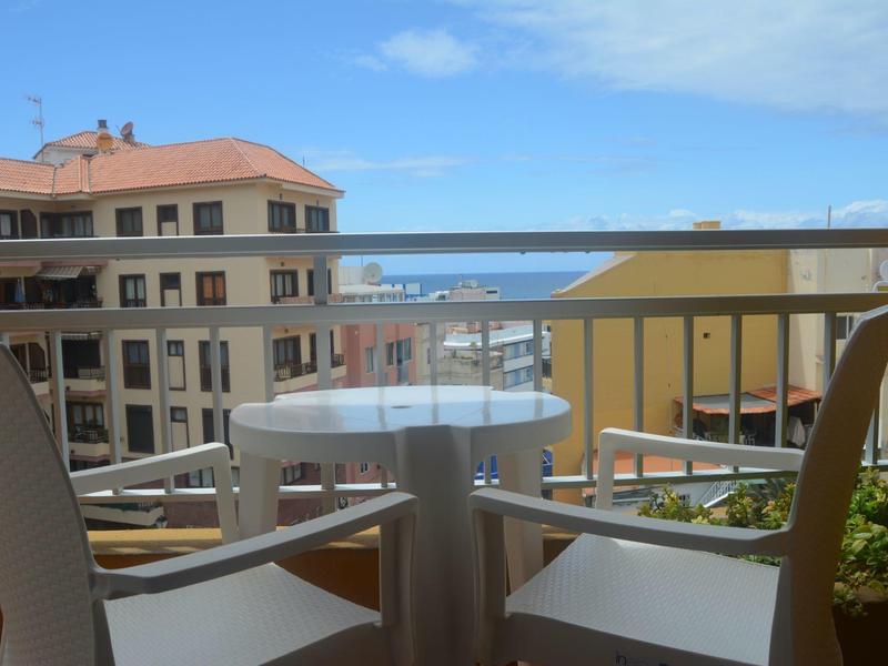 Balkon se stolem a židlemi s výhledem na okolní budovy a moře v pozadí.