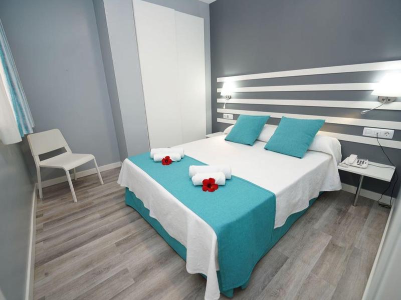 Moderně zařízený hotelový pokoj s manželskou postelí, modrými akcenty a židlí v rohu.