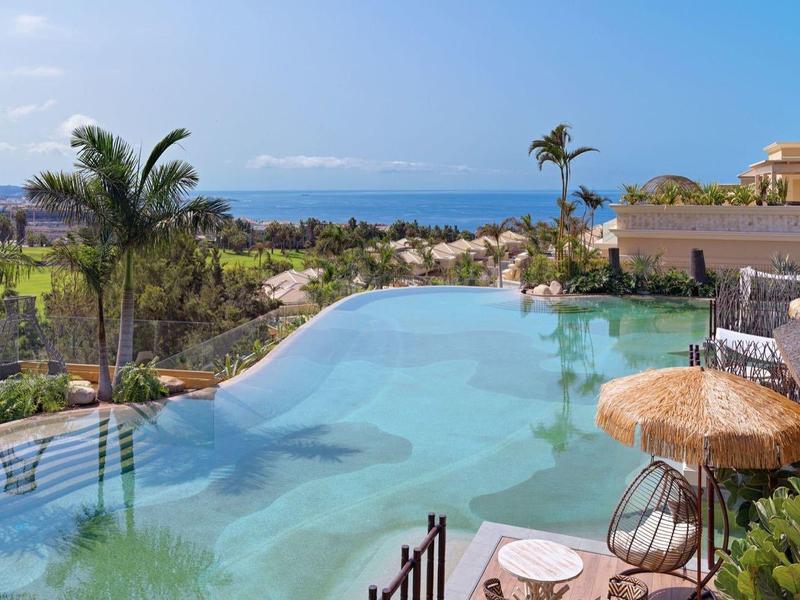 Infinity bazén s výhledem na moře, obklopený palmami a slunečními terasami.