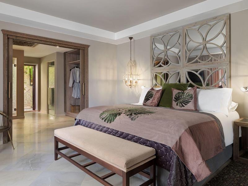 Elegantní ložnice s velkou postelí, dekorativními polštáři a lavicí na konci postele.