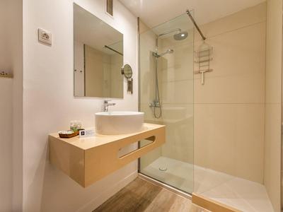 Nowoczesna łazienka z prysznicem typu walk-in, lustrem na ścianie i drewnianą umywalką.