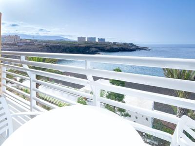 Widok z balkonu z białą balustradą na morze i wybrzeże pod bezchmurnym niebem.