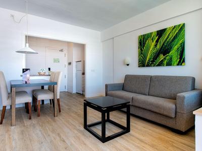 Salon moderne avec canapé gris, table à manger et décoration murale verte.