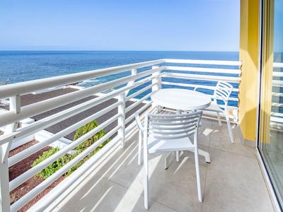 Balcon avec table blanche et chaises donnant sur la mer et le ciel bleu.