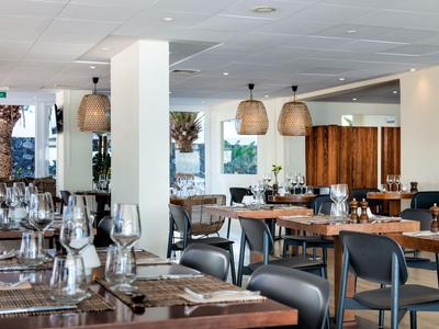 Restaurant moderne avec des tables en bois dressées et des chaises noires dans une ambiance lumineuse.